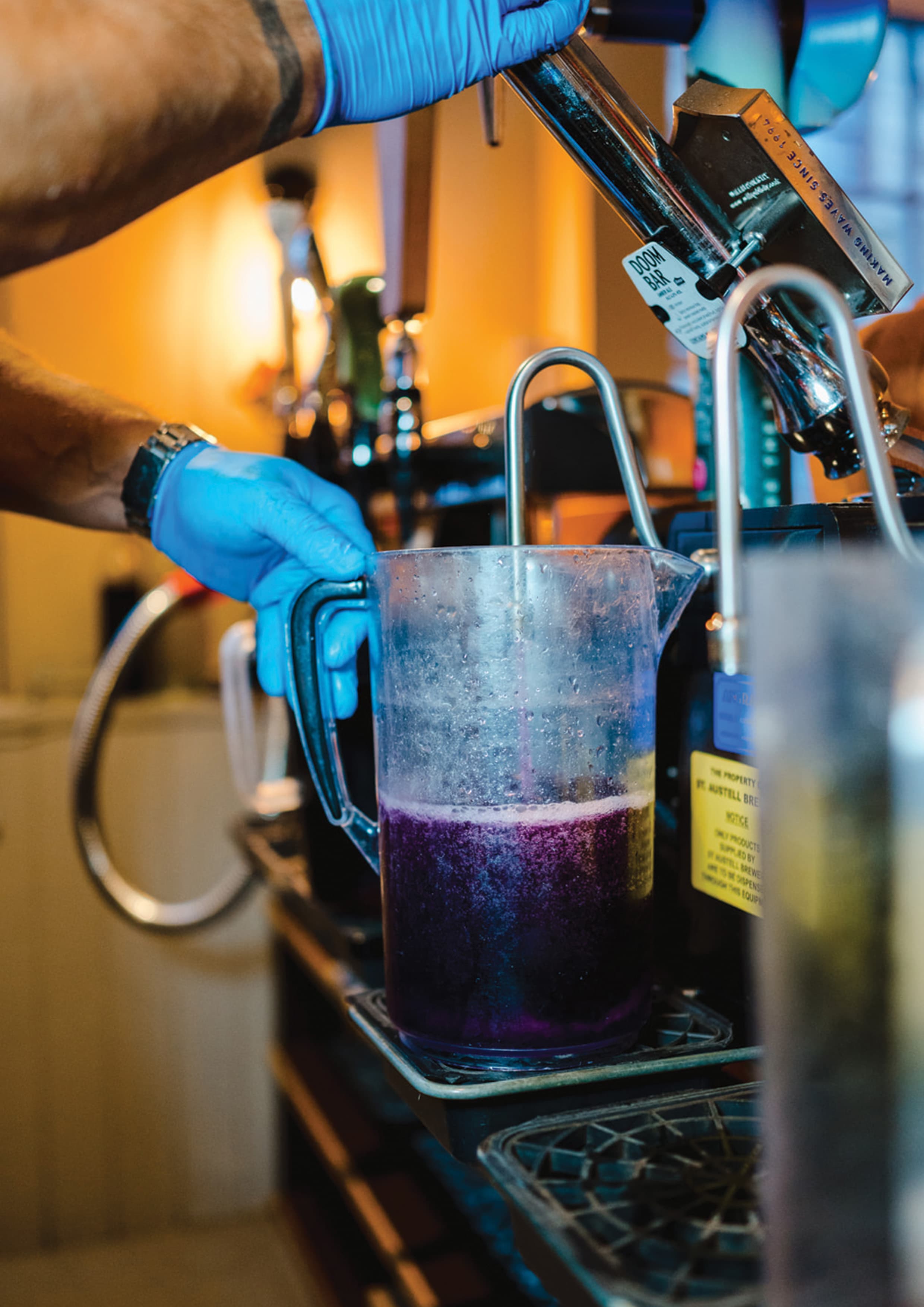 A Clear Brew engineer in blue gloves running cleaning fluid through a beer line into a jug at the tap